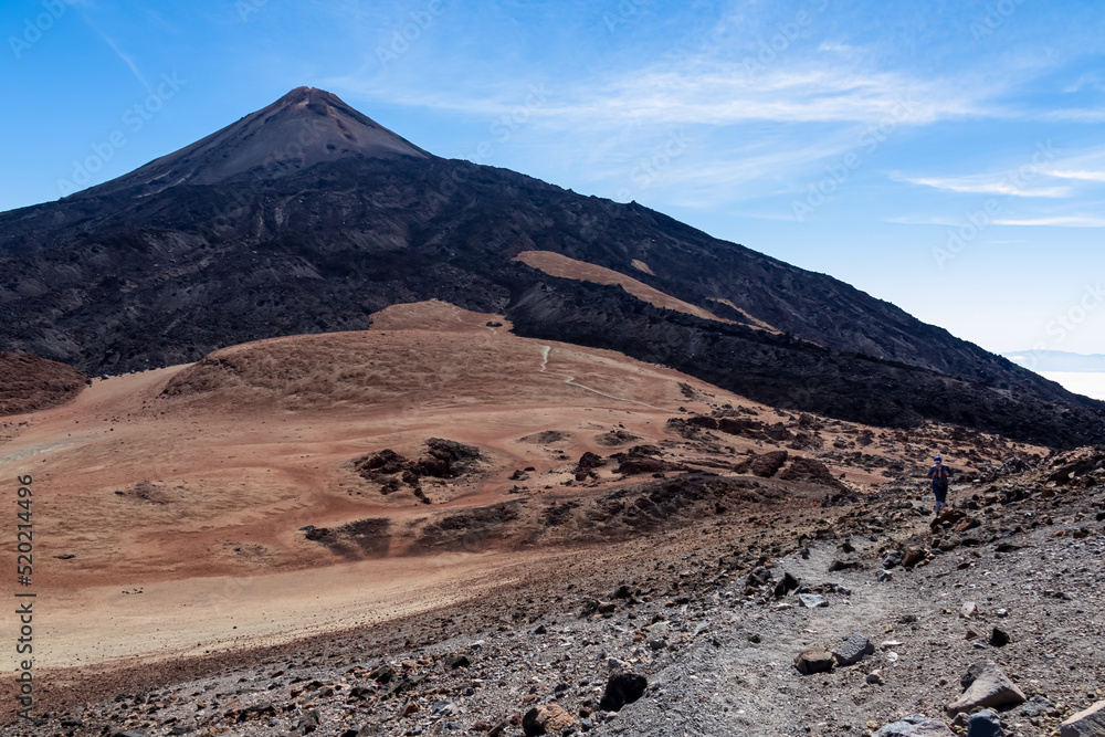 Woman on volcanic barren desert terrain hiking trail leading to summit of crater Pico Viejo, Tenerife, Canary Islands, Spain, Europe. Solidified lava, ash, pumice on path. Pico del Teide in the back