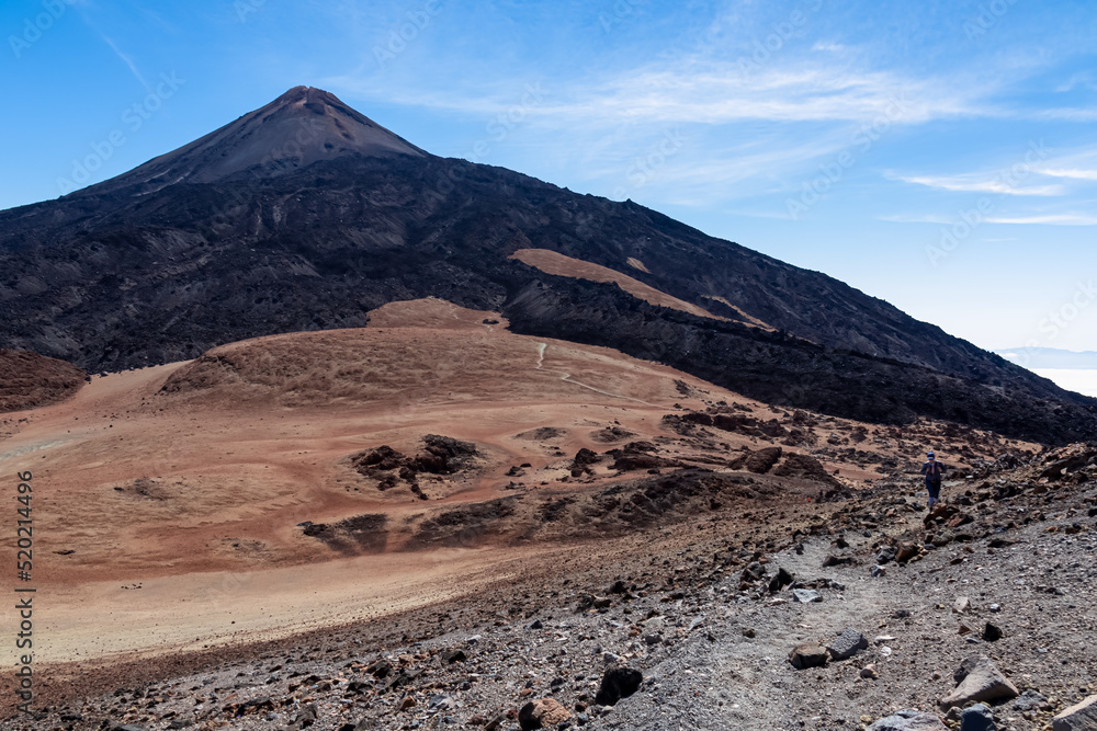 Woman on volcanic barren desert terrain hiking trail leading to summit of crater Pico Viejo, Tenerife, Canary Islands, Spain, Europe. Solidified lava, ash, pumice on path. Pico del Teide in the back Woman on volcanic barren desert terrain hiking trail leading to summit of crater Pico Viejo, Tenerife, Canary Islands, Spain, Europe. Solidified lava, ash, pumice on path. Pico del Teide in the back