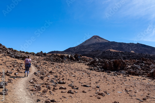 Woman with backpack on volcanic desert terrain hiking trail leading to summit volcano Pico del Teide  Mount Teide National Park  Tenerife  Canary Islands  Spain  Europe. Solidified lava  ash  pumice