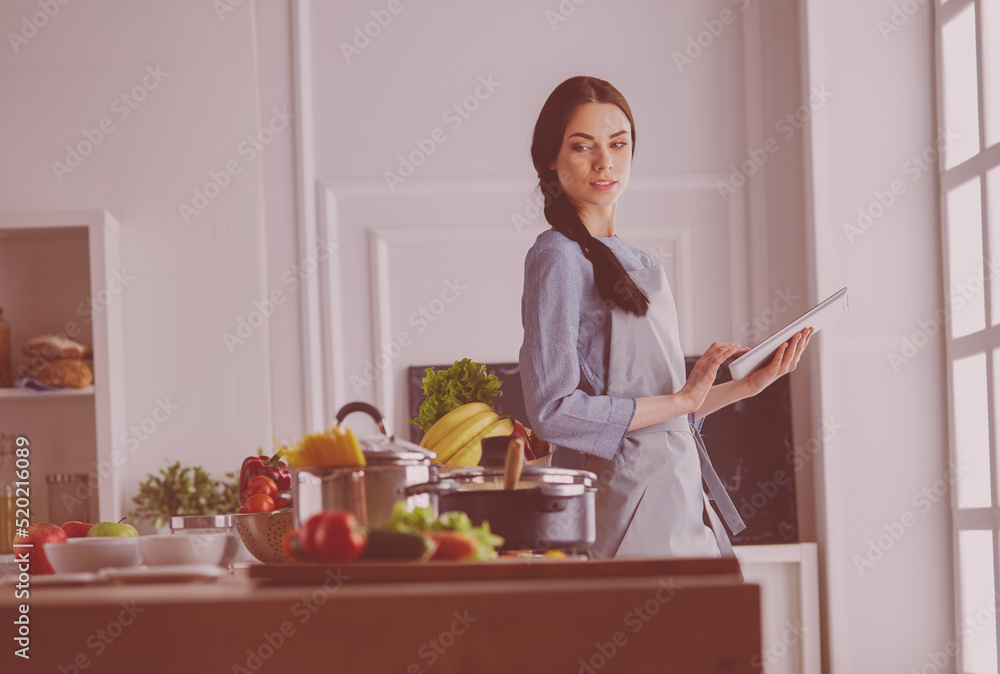 Young woman using a tablet computer to cook in her kitchen Young woman using a tablet computer to cook in her kitchen
