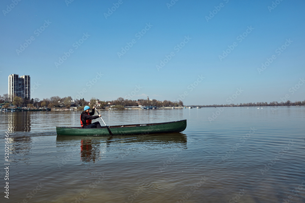 Man paddling in a canoe on a Danube river in urban area, small recreational escape, hobbies and sports outdoors.