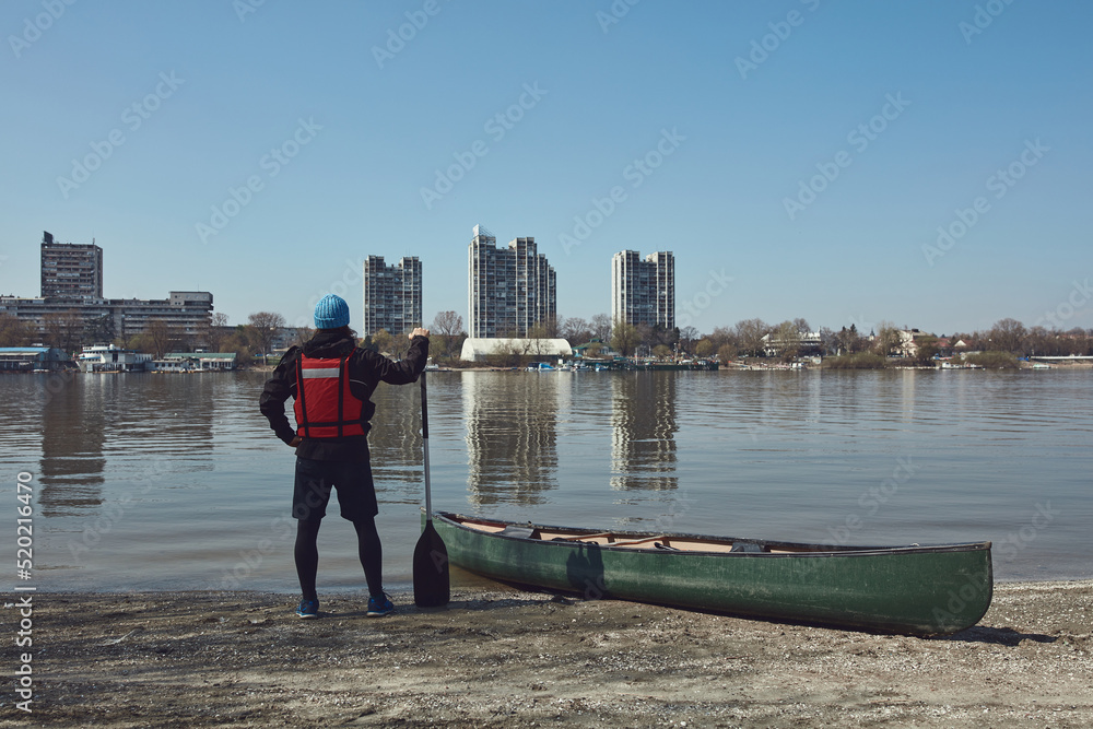 Man paddling with a canoe on a Danube river in urban area, small recreational escape, hobbies and sports outdoors.