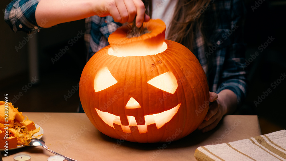Illuminated pumpkin for Halloween. Woman sitting and showing out candle