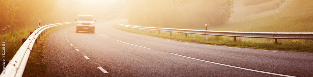 Fototapeta premium Black asphalt road with dividing line and safety fence in the morning mist.