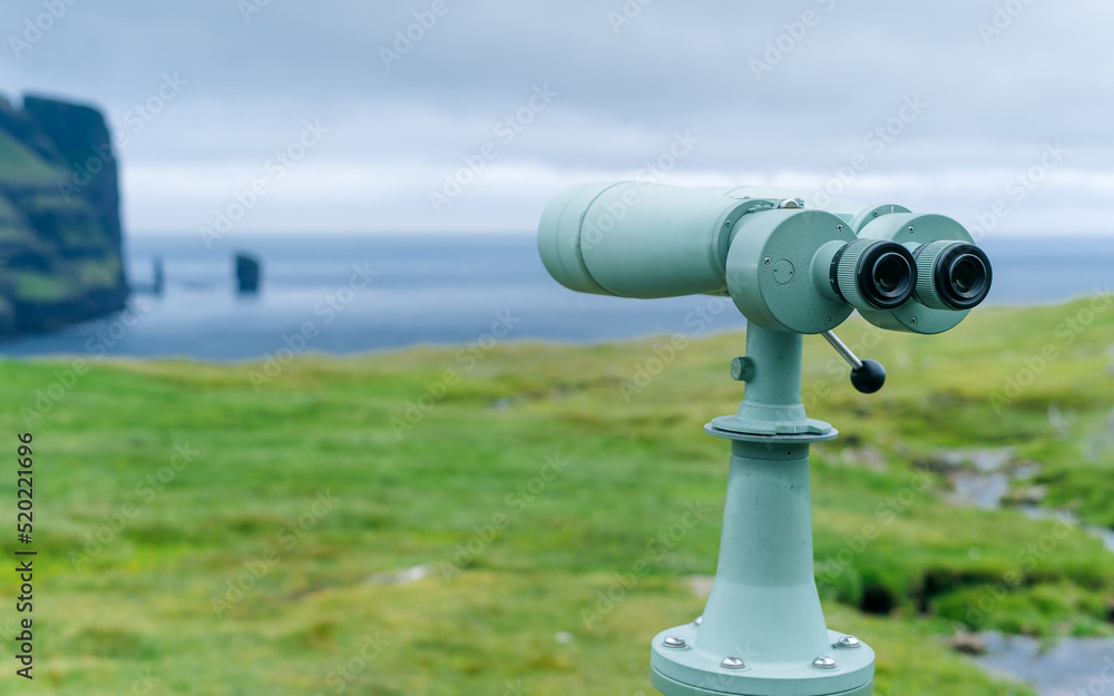 Touristic telescope look closeup binocular on background of popular tourist attraction - Risin og Kellingin cliffs. Viewpoint observe vision, metal coin operated in panorama observation, travel nature Touristic telescope look closeup binocular on background of popular tourist attraction - Risin og Kellingin cliffs. Viewpoint observe vision, metal coin operated in panorama observation, travel nature