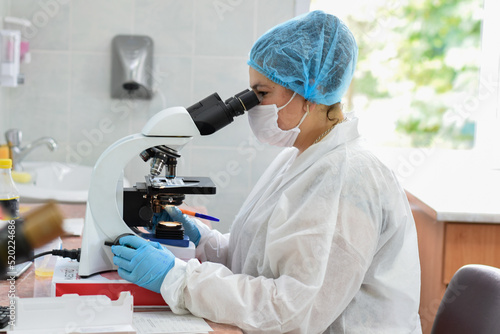 Female doctor analyzes under microscope in medical laboratory, analysis photo