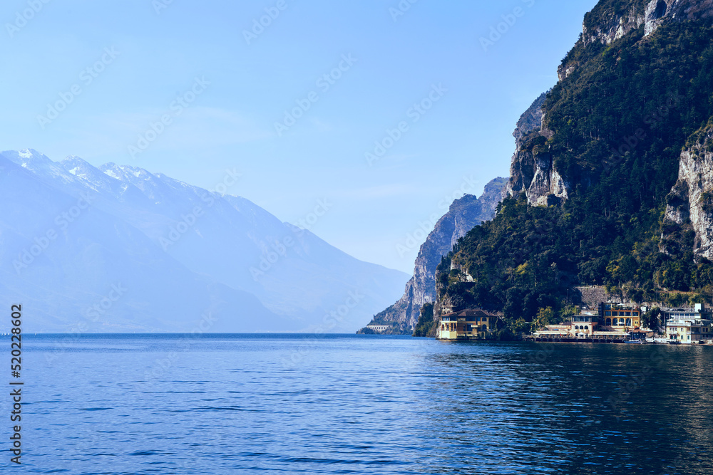 Garda lake viev on the open clean water surface with alpine mountain around and blue sky on the background