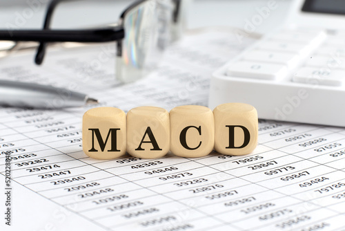 wooden cubes with the word MACD on a financial background with chart, calculator, pen and glasses, business concept.