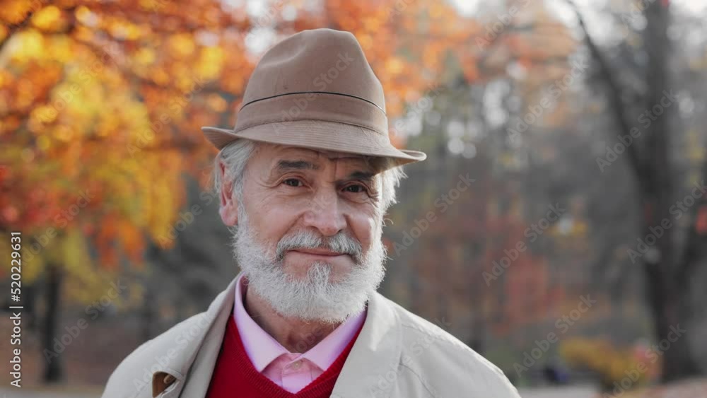 Portrait of handsome old grandfather looking at camera and smiling at autumn park. Close up of face of senior Caucasian man with gray hair and beard. Portrait of handsome old grandfather looking at camera and smiling at autumn park. Close up of face of senior Caucasian man with gray hair and beard.