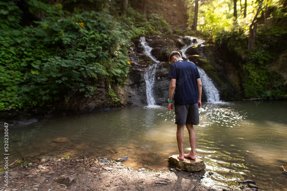 man stands near a waterfall in the middle of the forest man stands near a waterfall in the middle of the forest