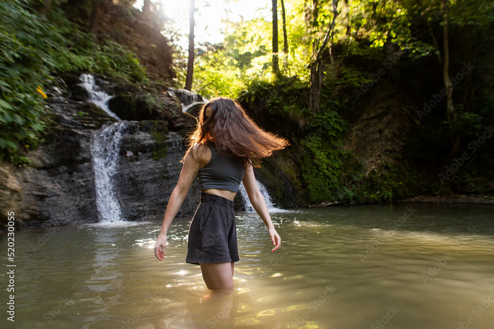 a young woman stands near a waterfall a young woman stands near a waterfall