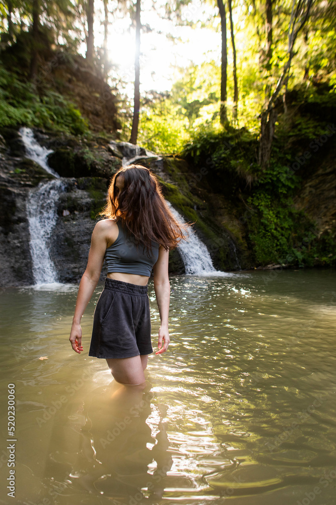 a young woman stands near a waterfall a young woman stands near a waterfall