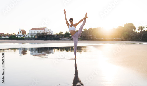 Caucasian woman in sportive wear doing yoga exercises for healthy vitality and wellness, flexible fit girl warming up and stretching body muscles during morning training at coastline with sunshine
