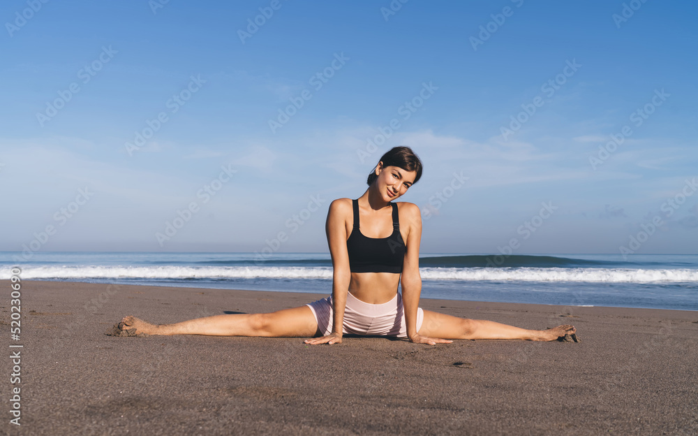 Flexible fit girl practice twine stretching during morning workout at coastline seashore beach, portrait of female in sportswear enjoying healthy lifestyle for body care warming up muscles in asana Flexible fit girl practice twine stretching during morning workout at coastline seashore beach, portrait of female in sportswear enjoying healthy lifestyle for body care warming up muscles in asana