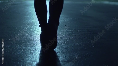 Legs of a man in backlight walking down the street at night.