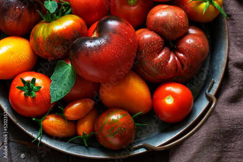 Tomatoes of various varieties and sizes on an iron tray on a wooden table.