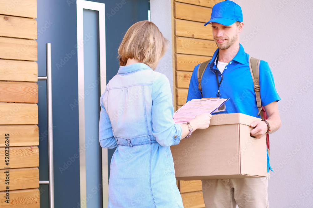 Smiling delivery man in blue uniform delivering parcel box to recipient - courier service concept. Smiling delivery man in blue uniform Smiling delivery man in blue uniform delivering parcel box to recipient - courier service concept. Smiling delivery man in blue uniform