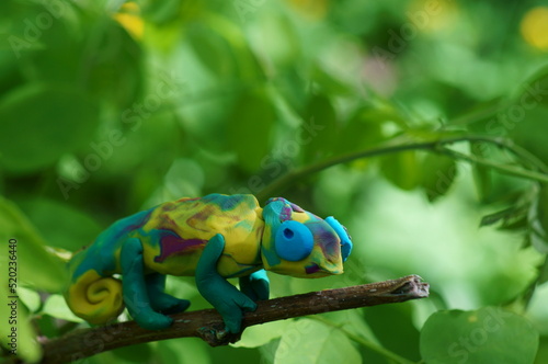 A toy colored chameleon on a tree branch. Animal figures.