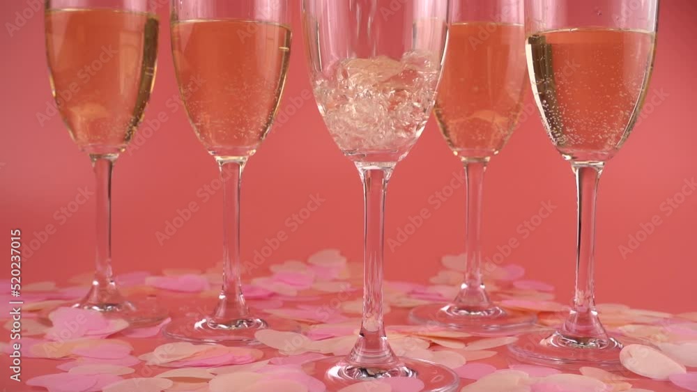 Pouring sparkling wine into glasses on a pink background with heart-shaped confetti. Slow motion. Pouring sparkling wine into glasses on a pink background with heart-shaped confetti. Slow motion.