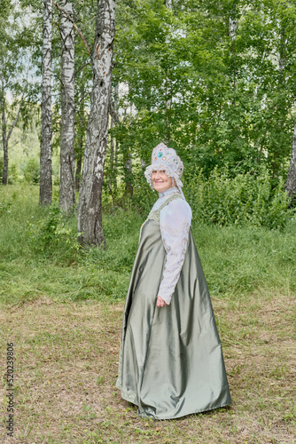 Smiling caucasian senior woman in stylized Russian traditional sundress and headdress, at rural.