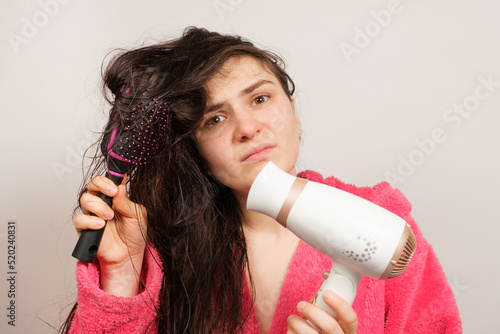 A brunette woman with matted hair dries it with a hair dryer. Hair care, overdried hair photo