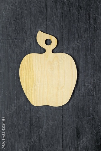 On a wooden table there is a board for cutting vegetables and fruits in the form of an apple