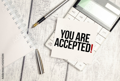 Text YOU ARE ACCEPTED on paper card and calculator on wooden background