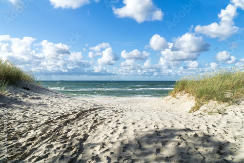 Entrance to a sandy beach through dunes, Baltic Sea near Łeba, Poland, Europe. Summer, little waves on the water, blue sky with white clouds.