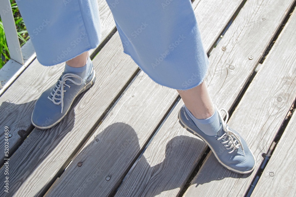 Women's legs in blue culottes and sneakers on a wooden bridge on a sunny summer day. Selective focus. Women's legs in blue culottes and sneakers on a wooden bridge on a sunny summer day. Selective focus.