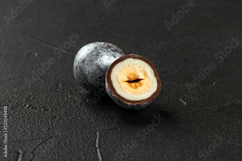Candy hazelnuts in chocolate with a cut half close-up on a dark concrete background