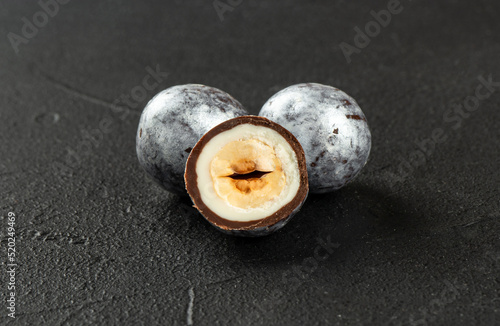 Two silver hazelnut candies in chocolate with a cut half close-up on a dark concrete background