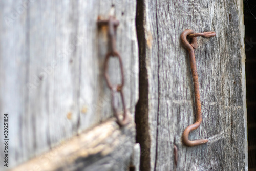 Isolated old rusty door latch on a wooden door. Close-up. Problematic weathered panels. Old wall texture background. Detail of an old wooden door with a rusty door latch.