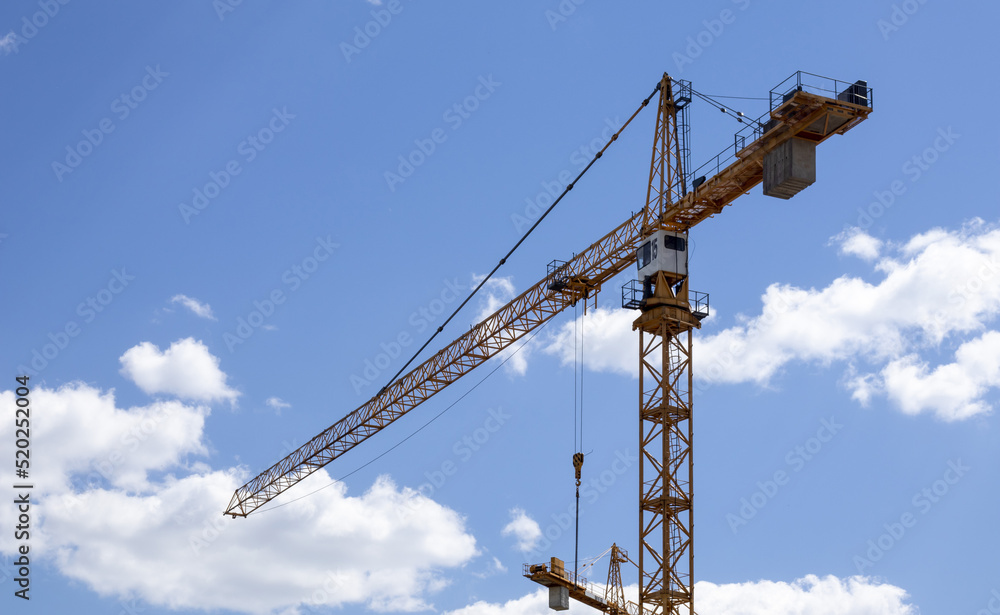 A working construction tower crane against a cloudy sky on a sunny day. The concept of urban development and construction. Industrial background. Crane engineering, construction industry tool.