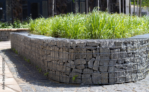 Basket support wall made of granite gabion. Gabions in the garden. Modern Gabion fence with stones in wire mesh. Gabion wire mesh fencing with natural stone and shrubs.