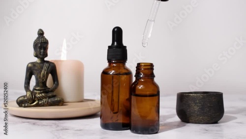 Spa treatment bottle of natural organic oil essence serum collagen. Aromatic candle and Buddha on white background. Beautiful woman hands.