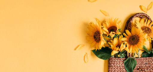 Summer or autumn background. Wicker bag with bouquet of sunflower flowers on yellow background. Flat lay, top view, copy space