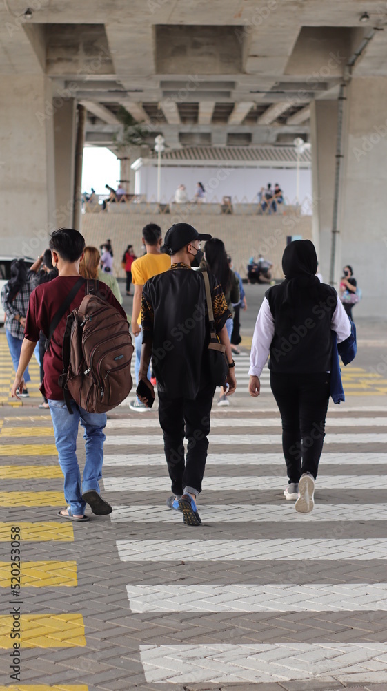 jakarta, indonesia - december, 2021 - three people crossing the street at a zebra cross jakarta, indonesia - december, 2021 - three people crossing the street at a zebra cross