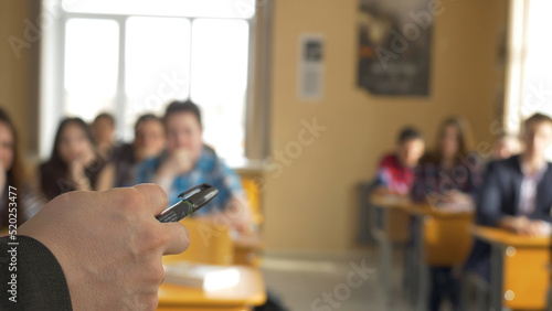 Teacher with a group of high school students in classroom. View from the hands of the teacher explaining the lecture