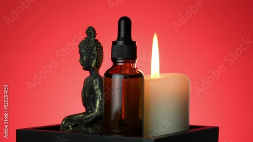Rotating statue of meditating Buddha and bottle of oil essence serum collagen with candle