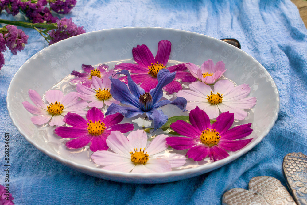 Cosmos and clitis flowers in a bowl of water, surrounded by flowers and ceramic hearts on a blue background Cosmos and clitis flowers in a bowl of water, surrounded by flowers and ceramic hearts on a blue background