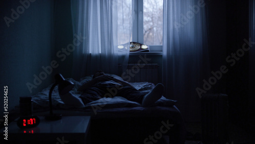 View of a man at night suffering from deep depression. Lonely man lying on the bed in the dark
