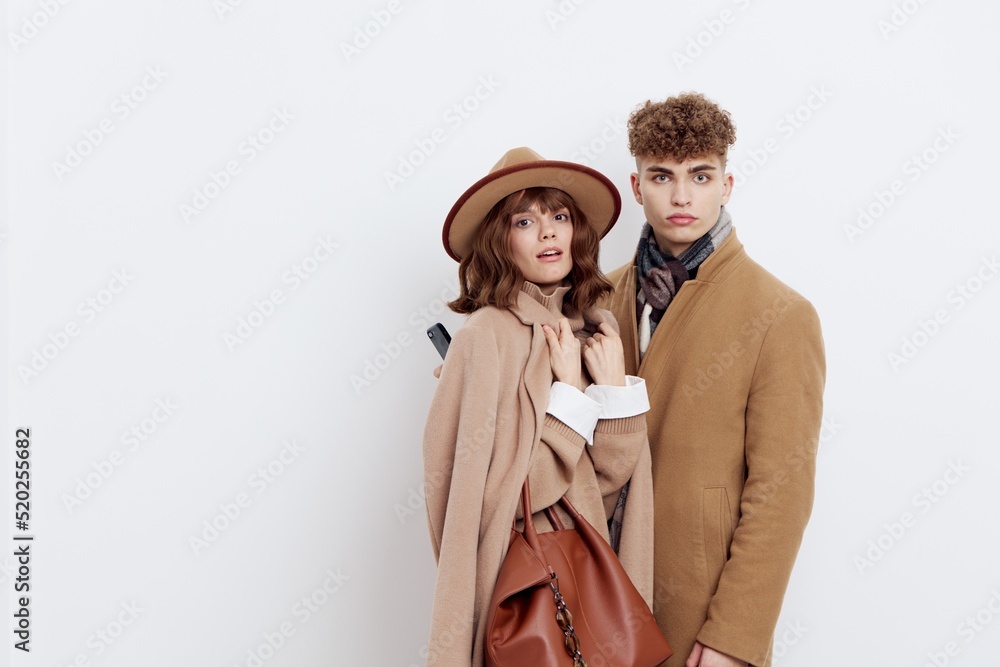 a stylish, loving couple, a man with and a woman are standing on a white background in an autumn coat, a woman has a hat on her head and she is holding a brown bag a stylish, loving couple, a man with and a woman are standing on a white background in an autumn coat, a woman has a hat on her head and she is holding a brown bag