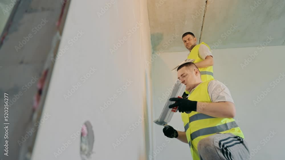 Two masters carry out repair work in the apartment. Specialists painters plasterer plastering the wall in the room. Two masters carry out repair work in the apartment. Specialists painters plasterer plastering the wall in the room.