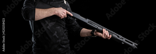 The man is holding a weapon. Pump-action 12 gauge shotgun isolated on a white background. A smooth-bore weapon with a plastic stock. Dark back.