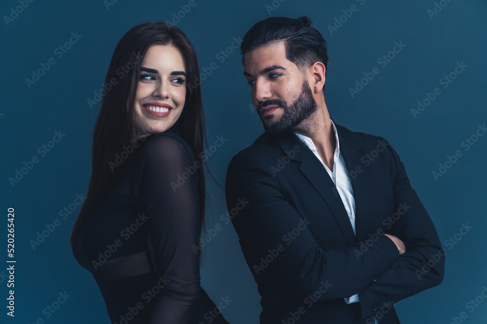 Young couple in black formal clothes standing back to back looking at each other flitring. Dark background studio shot. High quality photo Young couple in black formal clothes standing back to back looking at each other flitring. Dark background studio shot. High quality photo