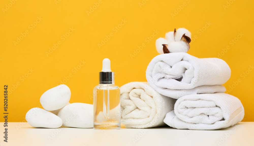 Glass bottle with a pipette and twisted white terry towels on the table Glass bottle with a pipette and twisted white terry towels on the table