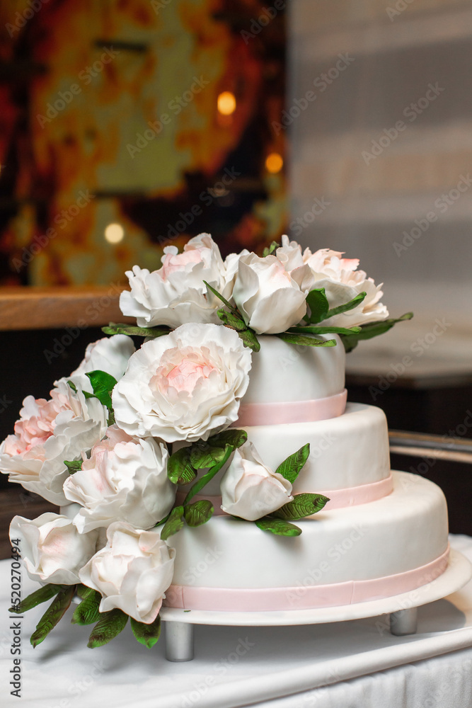 Multilevel wedding cake on the table decorated with roses Multilevel wedding cake on the table decorated with roses