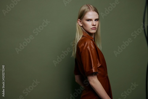 Cool portrait in studio with stylish professional blonde female model in trendy leather dress. Studio photoshoot in over olive green background © SHOTPRIME STUDIO
