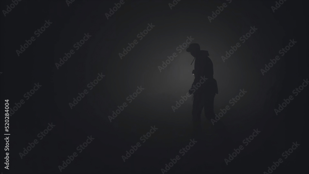 Silhouette of man in thick fog. Stock footage. Black silhouette of man with flashlight shining in thick grey smoke. Man with flashlight makes his way through darkness in smoke - obrazy, fototapety, plakaty 