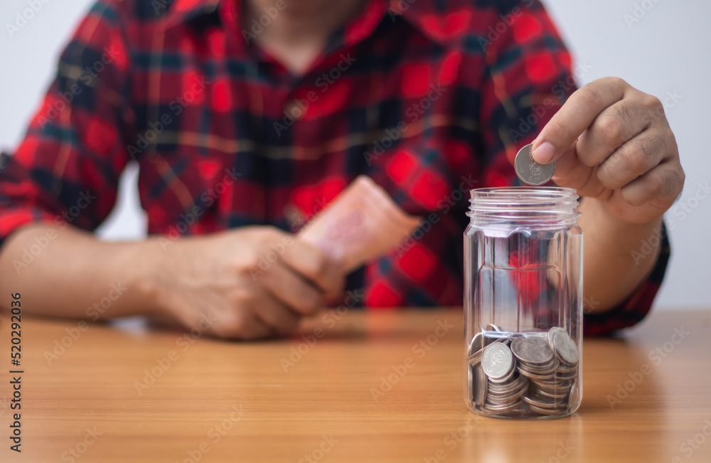 Man putting coin in clear plastic jar (Saving concept)
